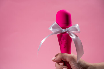 Woman holding pink vibrator with white bow on pink background. Copy space. 