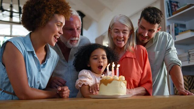 Multi-generation family celebrate granddaughter's birthday at home with cake singing Happy Birthday song as she blows out candles  - shot in slow motion