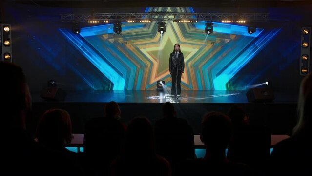 Young teenager girl singer performing on stage, contestant singing during recording of television style broadcast talent show