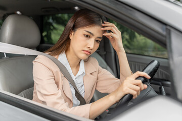 Tired young Asian woman with strong headache sitting in her car behind the wheel with seatbelt...