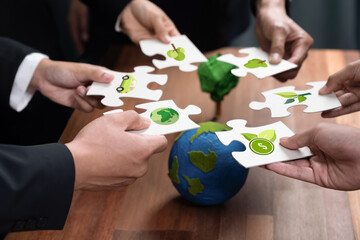Cohesive group of business people holding eco icon jigsaw puzzle pieces around globe Earth as eco...
