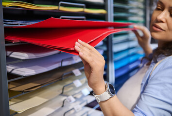 Focus on female hand choosing red color paper in stationery shop. Shopping school supply material....