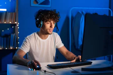 Fotobehang Gaming Young arabic gamer wearing headphones playing video game on personal computer, play in eSport cyber games tournament in neon light  © Andrii Lysenko