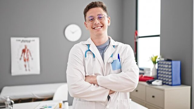 Young hispanic man doctor smiling confident standing with arms crossed gesture at clinic