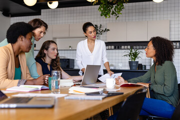Diverse female colleagues in discussion using laptop in casual meeting in office