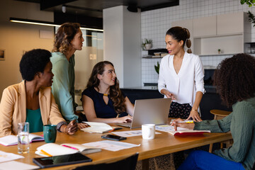 Diverse female colleagues in discussion using laptop in casual meeting in office