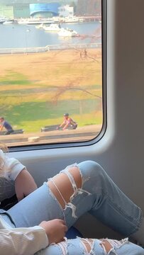 European girl with blond long hair in a white shirt rides in a skytrain The girl stands with her back to the camera 