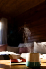 Vertical image of mug of fresh coffee and book on table in log cabin on sunny day