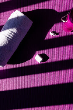 Vertical image of bottle of water, towel, earphones lying on mat on sunny day