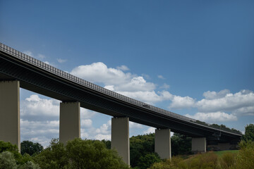 eine lange und hohe Brücke spannt sich über ein Tal  mit blauem Himmel und weißen Wolken