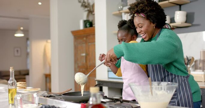 Happy african american mother and daughter frying pancakes in kitchen, slow motion