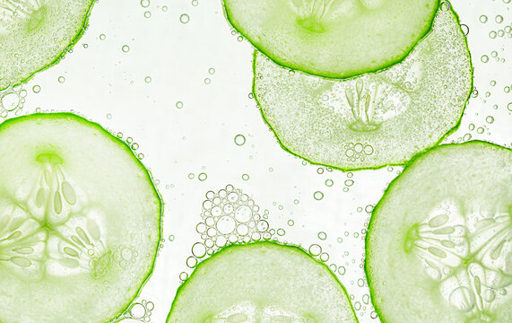 thinly sliced cucumber slices in water droplets on a light background. background for cosmetology and medicine