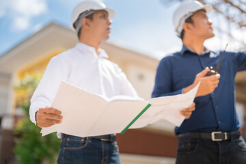 Close-up of blueprints in the hands of two Asian male engineers as master engineers and supervisors in construction business. About the architecture industry Wear uniforms, helmets and radios.