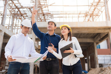 A team of 3 Asian male and female engineers at the construction site. View blueprint holding...