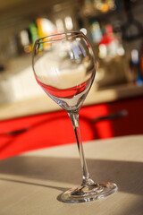 An empty wine glass on the kitchen table in a sunny day with sharp shadows and red reflection