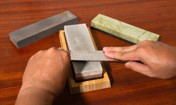 Craftsman sharpening knives on a Japanese whetstone, on a wooden table