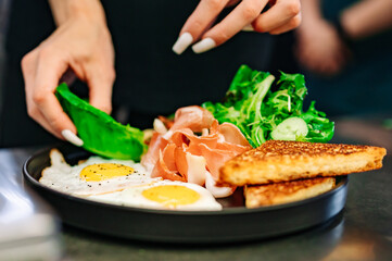 woman chef hand cooking fried eggs with ham, salad and hummus