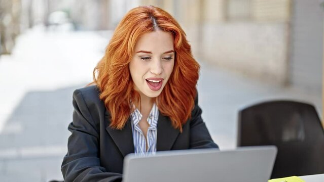 Young redhead woman business worker using laptop with winner expression at coffee shop terrace