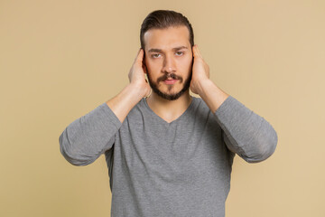 Dont want to hear and listen. Frustrated annoyed irritated lebanese man covering ears gesturing No, avoiding advice ignoring unpleasant noise loud voices. Middle eastern guy alone on beige background