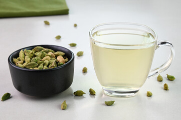 Cardamom water in a glass cup with cardamoms placed in a bowl.