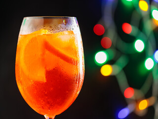 Glass of Aperol Spritz cocktail on a blurred background with colorful bokeh. Aperol spritz cocktail, close up. Alcoholic cocktail concept at a party. Copy space