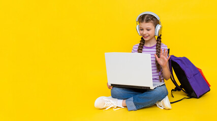 The child is engaged in an online lesson with a laptop. A young girl is sitting cross-legged on the...