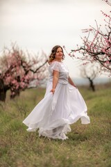 Obraz na płótnie Canvas Woman peach blossom. Happy woman in white dress walking in the garden of blossoming peach trees in spring