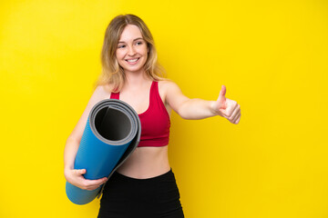 Young sport caucasian woman going to yoga classes while holding a mat isolated on yellow background giving a thumbs up gesture