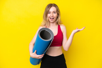 Young sport caucasian woman going to yoga classes while holding a mat isolated on yellow background with shocked facial expression