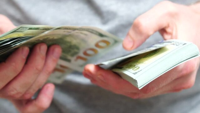 Male hands counting a stack of hundred-dollar US banknotes. Concept of investment, money exchange, financial transactions or business negotiations. Selective focus. Close-up. Slow motion