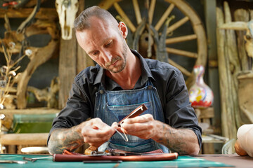 A leather craftsman is working hard to sew a leather product for a customer.