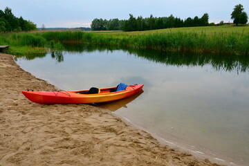 A view of a colorful, bright kayak or canoe with paddles and other equipment parked on a sandy...