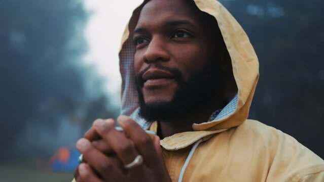 Coffee, morning and a black man hiking in nature with a blurred background of cold, winter weather. Thinking, raincoat and face with a young male hiker in the woods or forest to explore for adventure