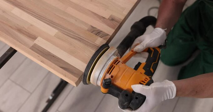 Carpenter sanding wood with sandpaper in carpentry or workshop. Electric grinder works in carpentry