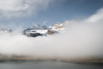 Fototapeta na wymiar The snowy peaks of Mount Bernina appear from the low clouds above the Lago Bianco