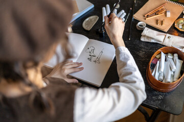 Illustrator hands drawing in notebook with black ink fantasy art. Designer freelancer preparing...