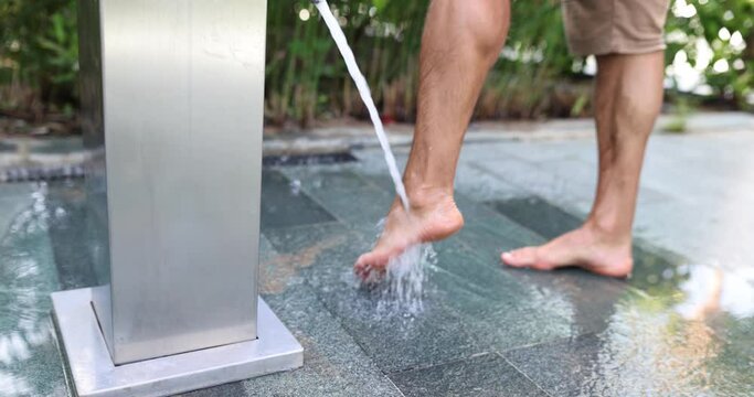 Man washing his feet from sand under shower on sea beach closeup