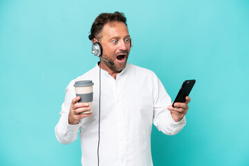Telemarketer caucasian man working with a headset isolated on blue background holding coffee to take away and a mobile