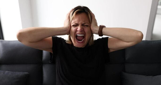 Young woman arguing and screaming angrily reacting to depression. Hysterical angry young woman broken on sofa