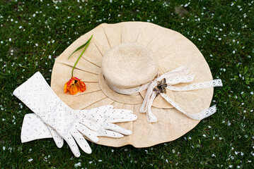 Lady's retro accessories on the green lawn covered with white petals (top view). White gloves,...