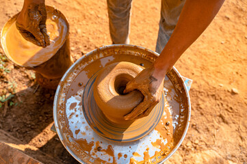 Potter making clay pot by using hand on the electric pottery, giving shape to the pot and one hand near muddy water bucket to take water from it during morning light.
