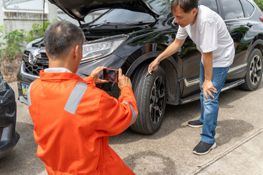 A car insurance agent taking a picture of a damaged mark on the car's tire while the custmer pointing it out with a pen