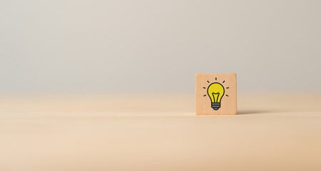 Idea and creativity concept. Wooden cube block with yellow light bulb icon on grey background....