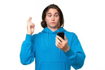 Young handsome man isolated on green chroma background using mobile phone with fingers crossing