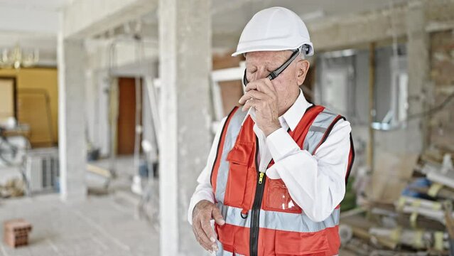 Senior grey-haired man architect stressed taking off hardhat at construction site