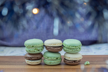 Close up delicious macaroon cookies in fresh mint green vanilla beige chocolate brown colors. Blue bokeh shining blurred foreground decor, wooden table. Contrast bright combination, bakery culinary.