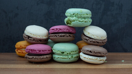 Close up delicious macaroon cookies in fresh mint green vanilla beige chocolate brown orange and pink colors. Dark gray background, wooden textured table. Contrast bright combination, bakery culinary.