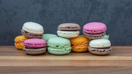 Close up delicious macaroon cookies in fresh mint green vanilla beige chocolate brown orange and pink colors. Dark gray background, wooden textured table. Contrast bright combination, bakery culinary.