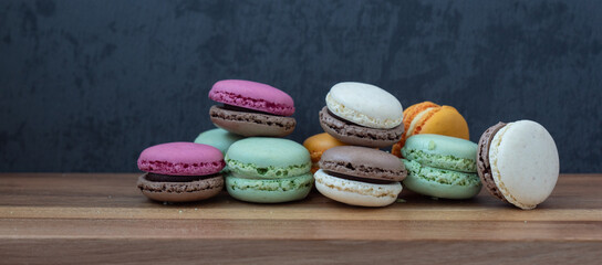 Close up delicious macaroon cookies in fresh mint green vanilla beige chocolate brown orange and pink colors. Dark gray background, wooden textured table. Contrast bright combination, bakery culinary.