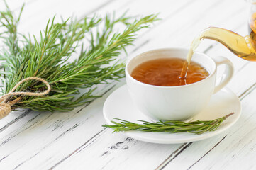 Glass cup of healthy rosemary tea with fresh rosemary bunch on rustic background, winter herbal hot drink concept, salvia rosmarinus